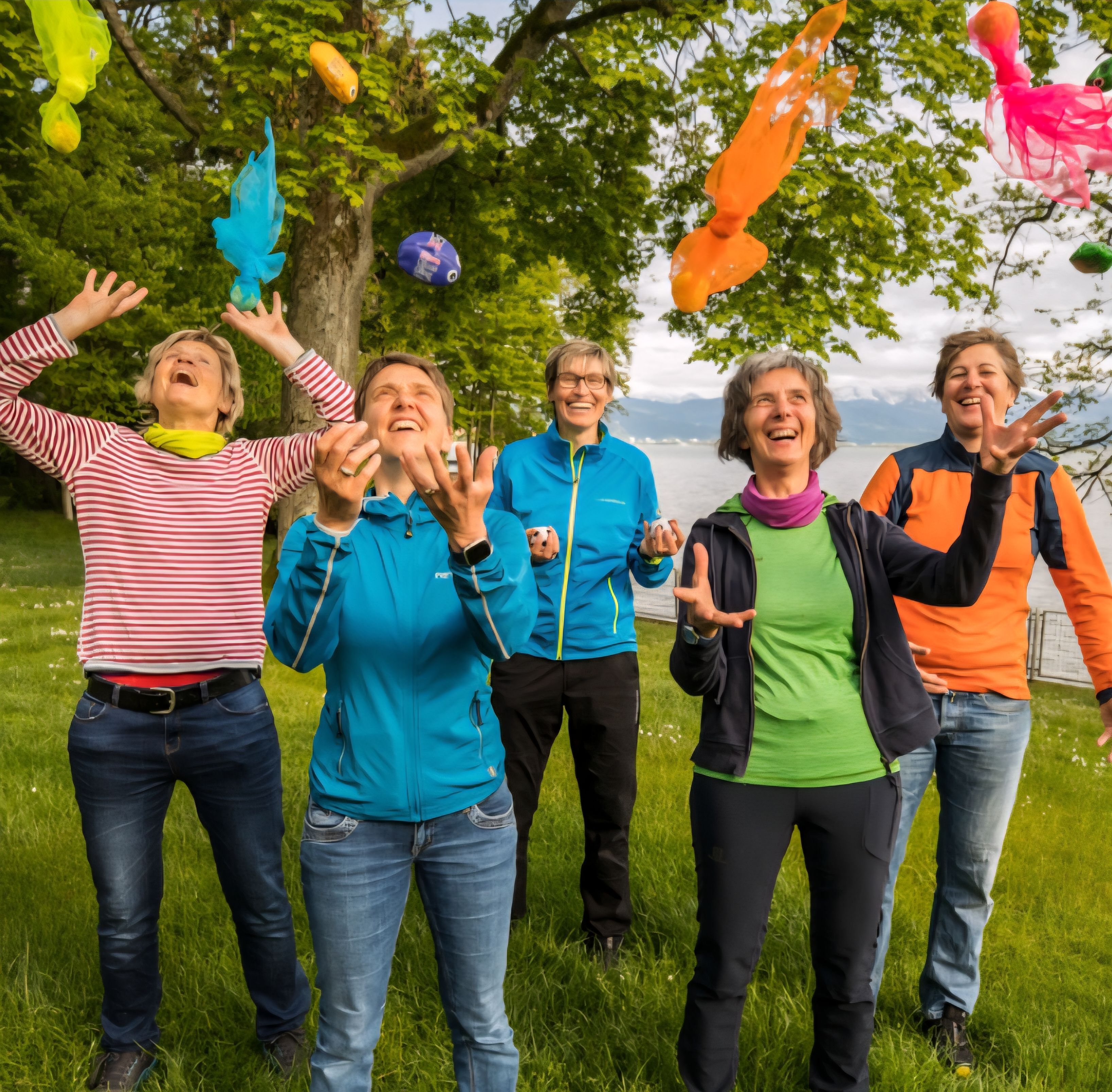 Foto von fünf Frauen auf einer Wiese, die verschiedene Bälle und Tücher in die Luft werfen und dabei lachen.
