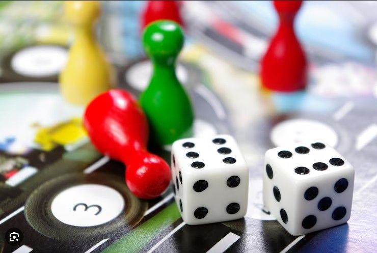 Das Bild zeigt zwei W&uuml;rfel und rote,gr&uuml;ne und gelbe Spielfiguren auf einem angedeuteten Spielfeld